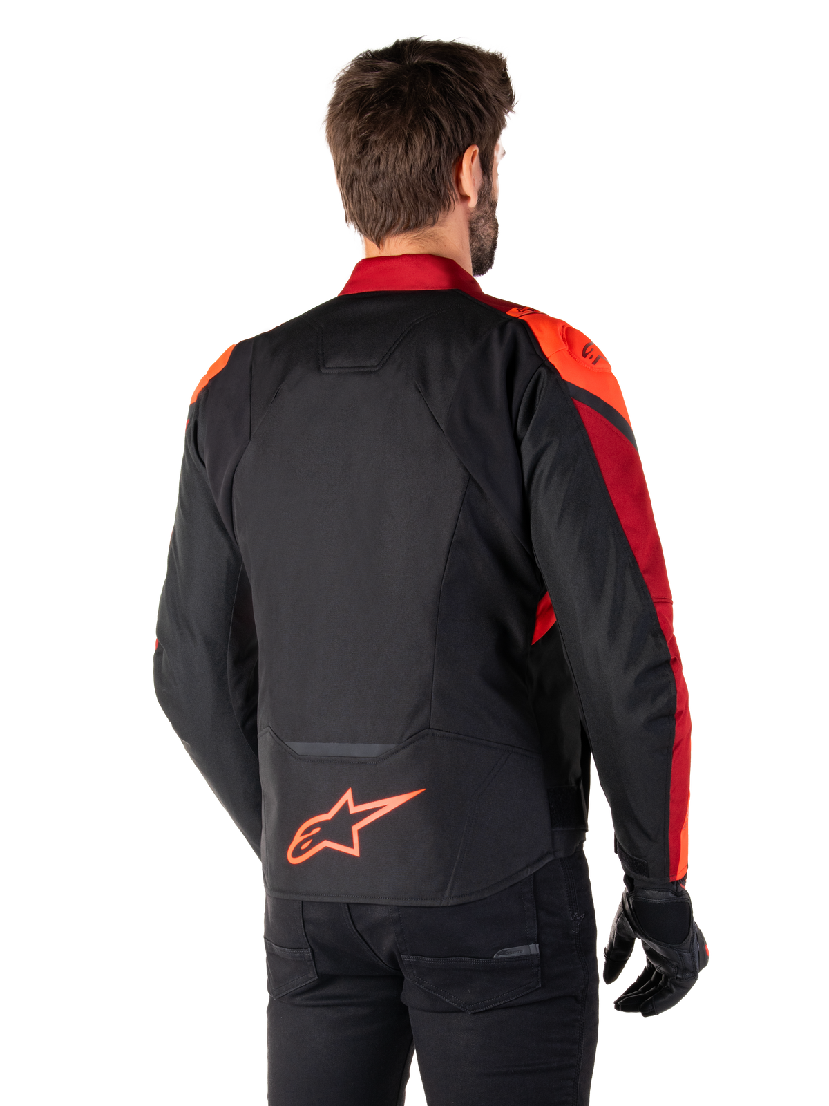 Achteraanzicht van een man die de Alpinestars T-Jaws V4 Waterproof Jas draagt in Black Red Fluo Dark Red, met opvallende rode accenten op de schouders en mouwen, een fluo rood Alpinestars-logo op de onderrug, gecombineerd met een zwarte broek en handschoenen.