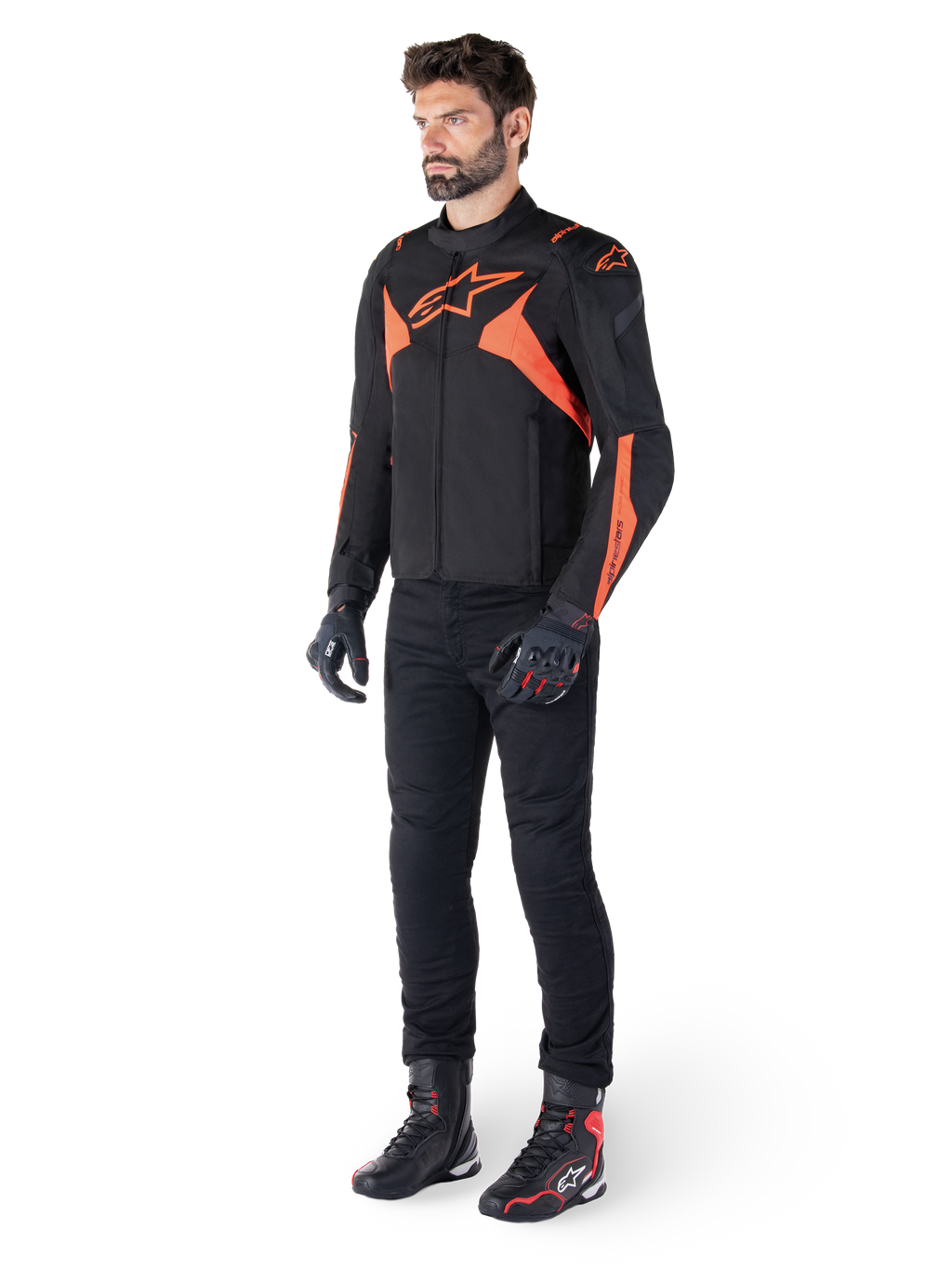 Alpinestars T-Jaws V4 waterdichte jas, zwart en fluo rood, gedragen door een mannelijk model met zwarte broek, handschoenen en laarzen, voorzien van felle oranje accenten en het Alpinestars-logo, sportief ontwerp voor motorrijden