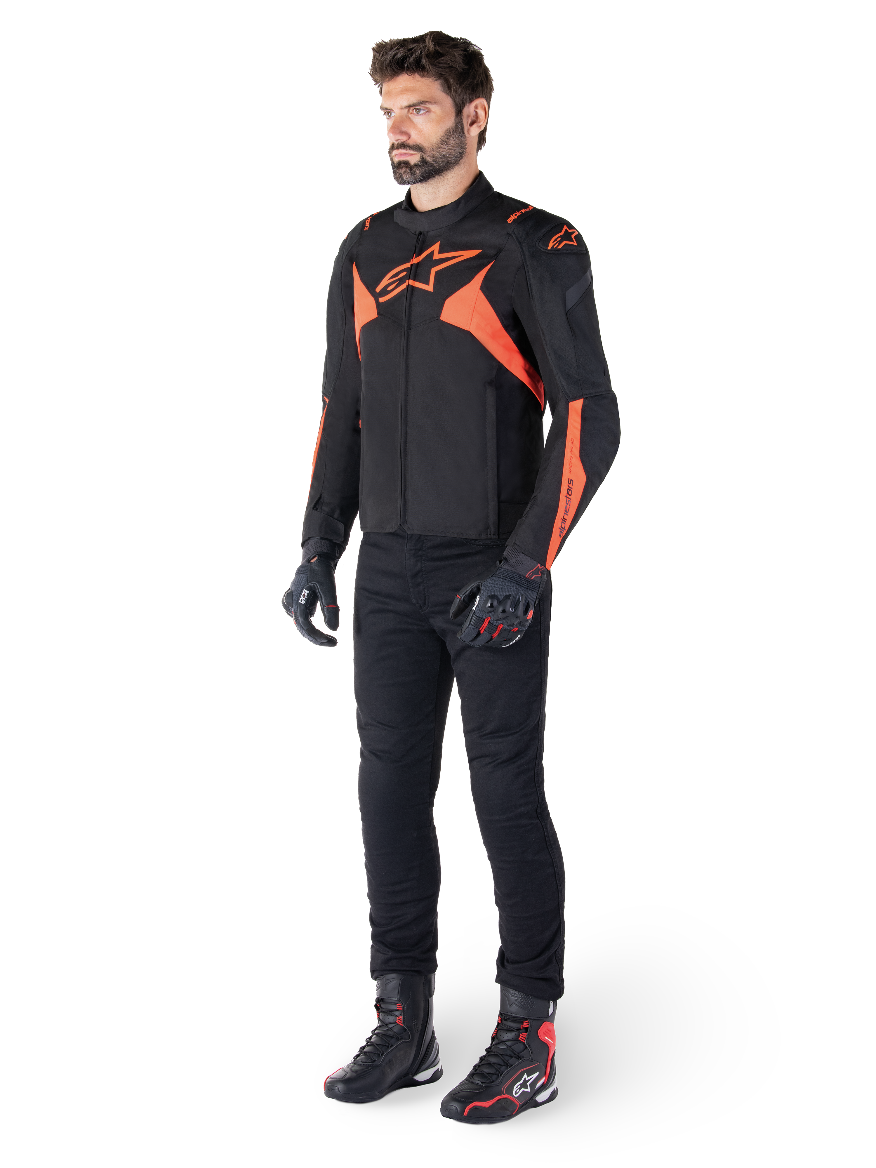 Alpinestars T-Jaws V4 waterdichte jas, zwart en fluo rood, gedragen door een mannelijk model met zwarte broek, handschoenen en laarzen, voorzien van felle oranje accenten en het Alpinestars-logo, sportief ontwerp voor motorrijden