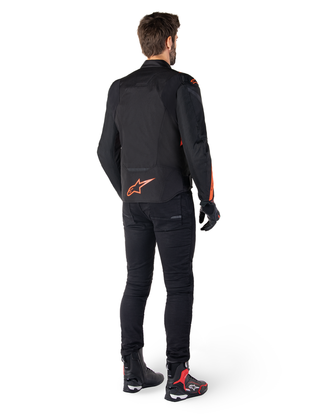 Alpinestars T-Jaws V4 Waterproof Jacket, zwart en rood fluo, achteraanzicht gedragen door een mannelijke motorrijder, voorzien van een opvallend fluorood logo op de rug, gecombineerd met een zwarte motorbroek en technische laarzen, sportieve motorkleding