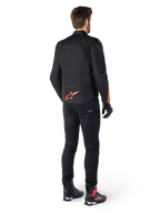 Alpinestars T-Jaws V4 Waterproof Jacket, zwart en rood fluo, achteraanzicht gedragen door een mannelijke motorrijder, voorzien van een opvallend fluorood logo op de rug, gecombineerd met een zwarte motorbroek en technische laarzen, sportieve motorkleding