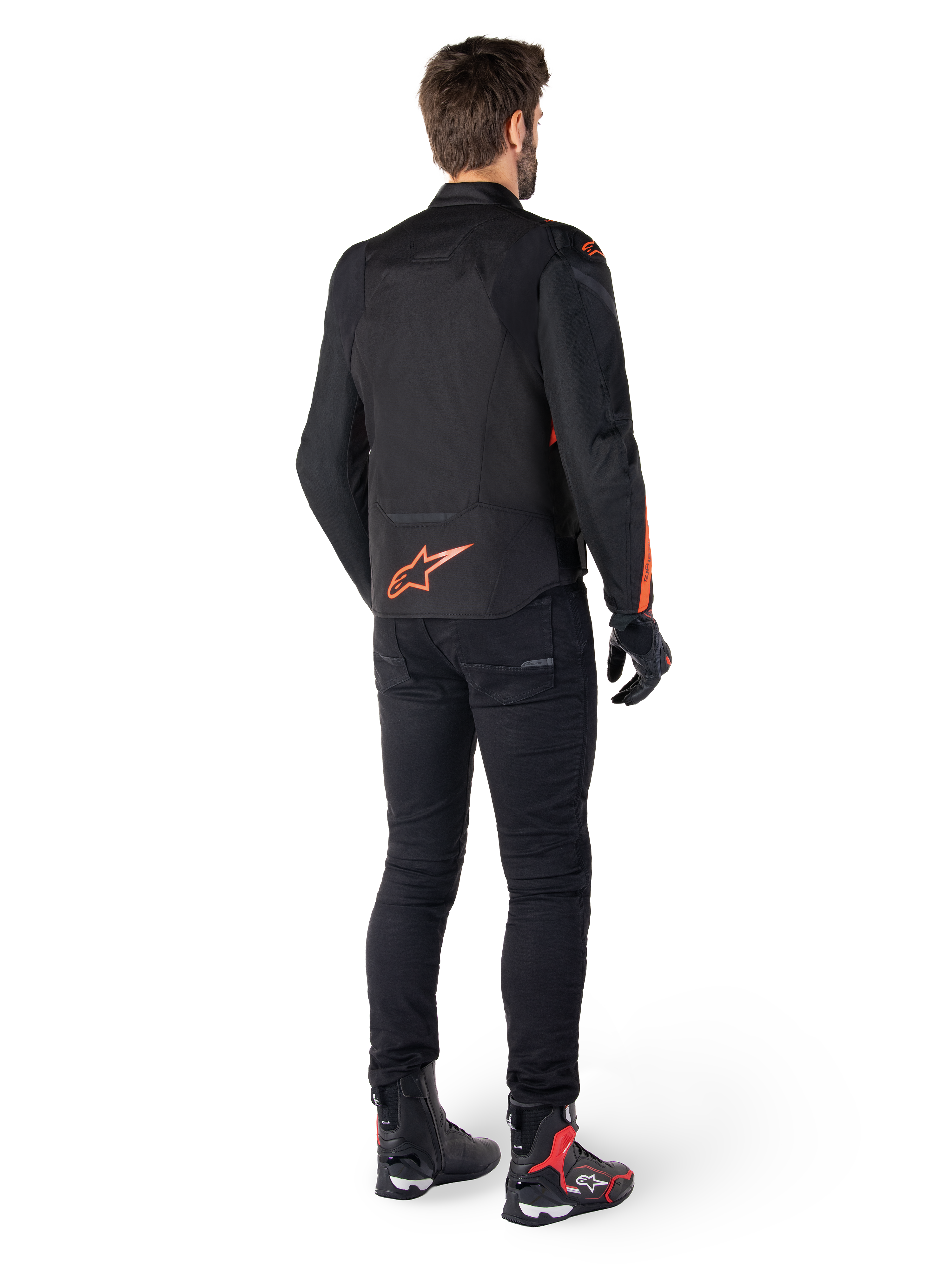 Alpinestars T-Jaws V4 Waterproof Jacket, zwart en rood fluo, achteraanzicht gedragen door een mannelijke motorrijder, voorzien van een opvallend fluorood logo op de rug, gecombineerd met een zwarte motorbroek en technische laarzen, sportieve motorkleding
