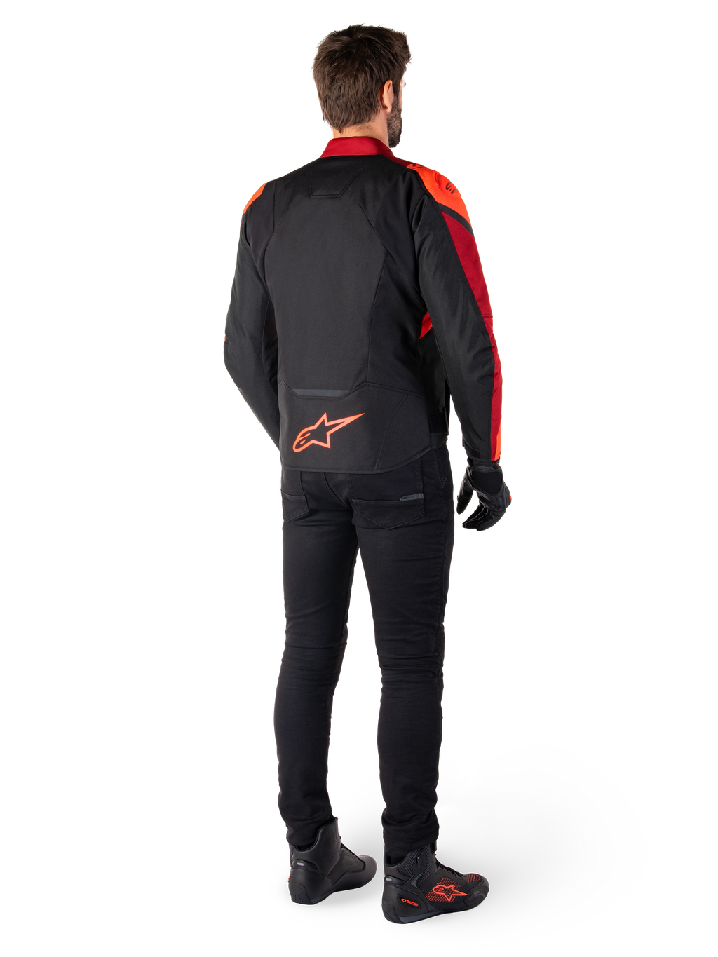 Alpinestars T-Jaws V4 Waterproof Jas in Black Red Fluo Dark Red, achteraanzicht van een motorrijder die de textiele jas draagt met een zwarte broek en motorlaarzen, voorzien van een opvallend rood Alpinestars-logo op de onderrug.