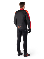 Alpinestars T-Jaws V4 Waterproof Jas in Black Red Fluo Dark Red, achteraanzicht van een motorrijder die de textiele jas draagt met een zwarte broek en motorlaarzen, voorzien van een opvallend rood Alpinestars-logo op de onderrug.