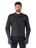 Alpinestars T-Jaws V4 Waterproof Jacket, zwarte sportieve motorjas, gedragen door een man met zwarte handschoenen met rode accenten, versterkte schouders en armen, gestroomlijnd design met subtiel logo op de borst, textiele all-weather motorkleding