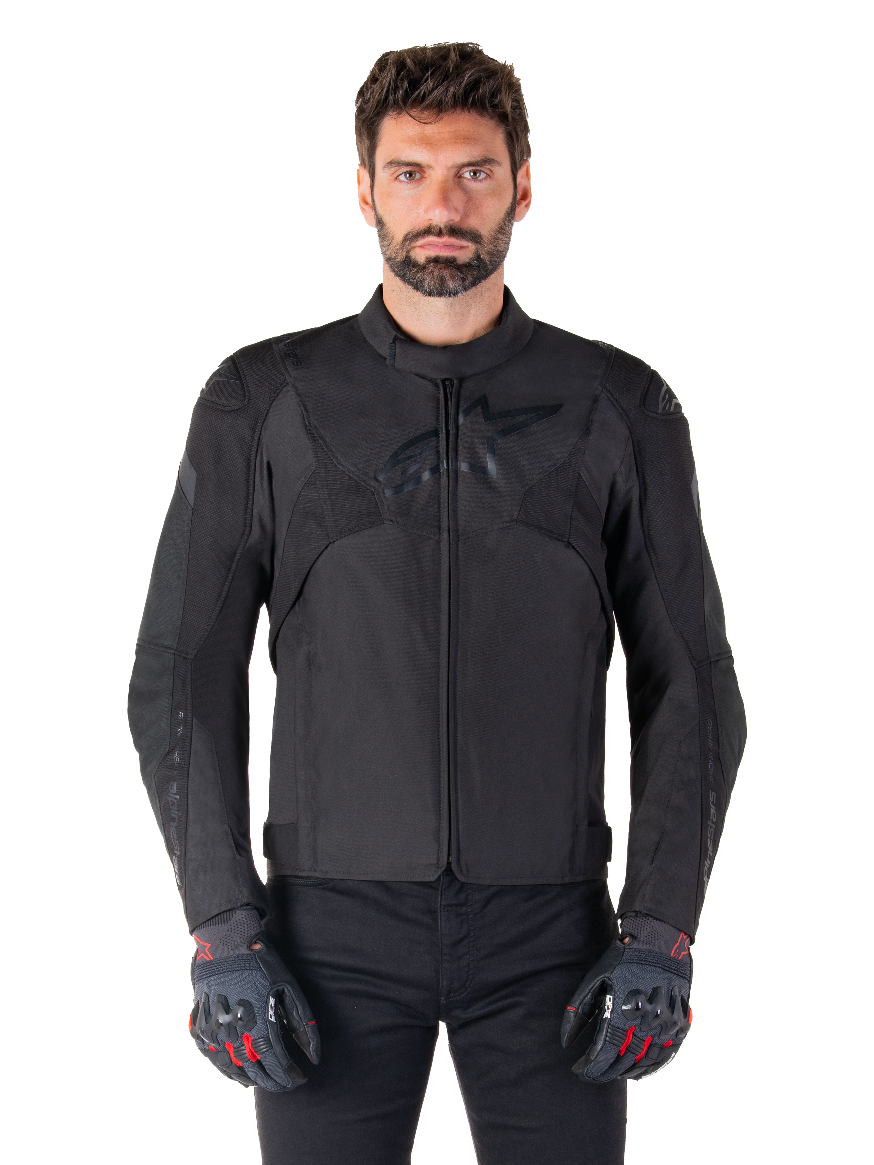 Alpinestars T-Jaws V4 Waterproof Jacket, zwarte sportieve motorjas, gedragen door een man met zwarte handschoenen met rode accenten, versterkte schouders en armen, gestroomlijnd design met subtiel logo op de borst, textiele all-weather motorkleding