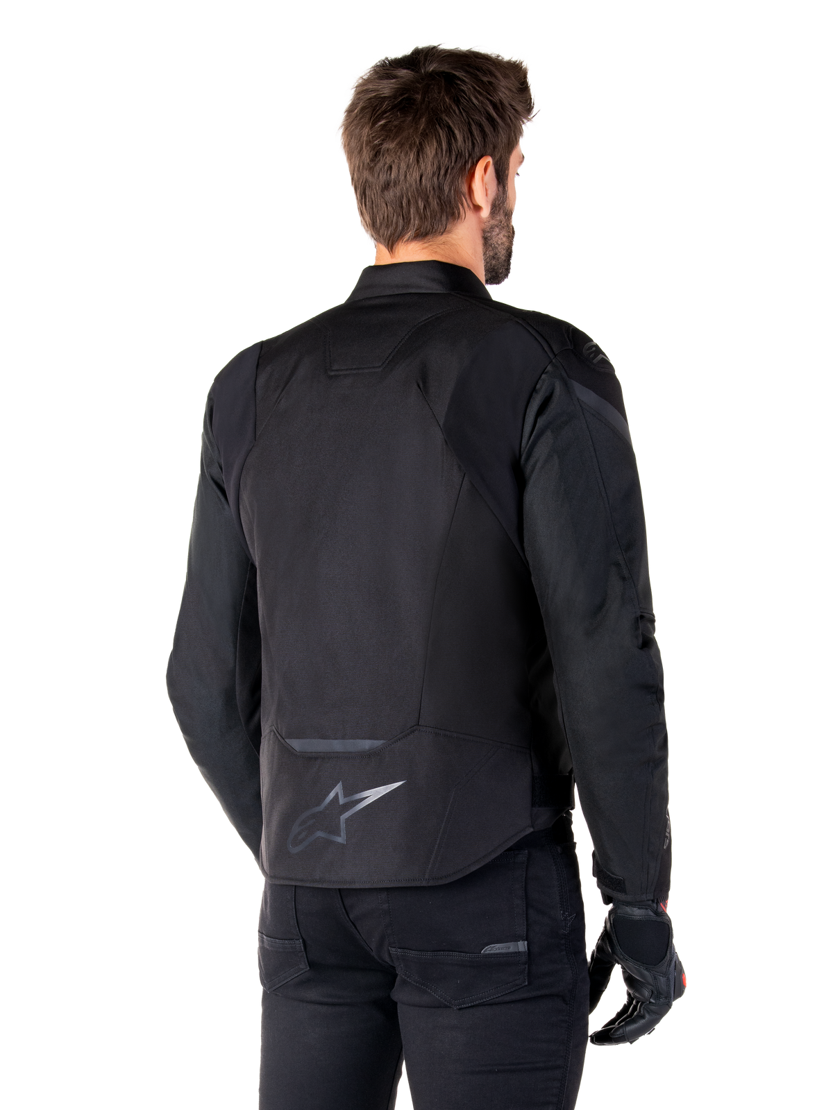 Alpinestars T-Jaws V4 Waterproof Jacket, zwart, achteraanzicht op model, met een reflecterend Alpinestars-logo op de onderrug, verlengde achterkant voor extra dekking, sportief textielontwerp met tonale panelen, gedragen met zwarte motorhandschoenen