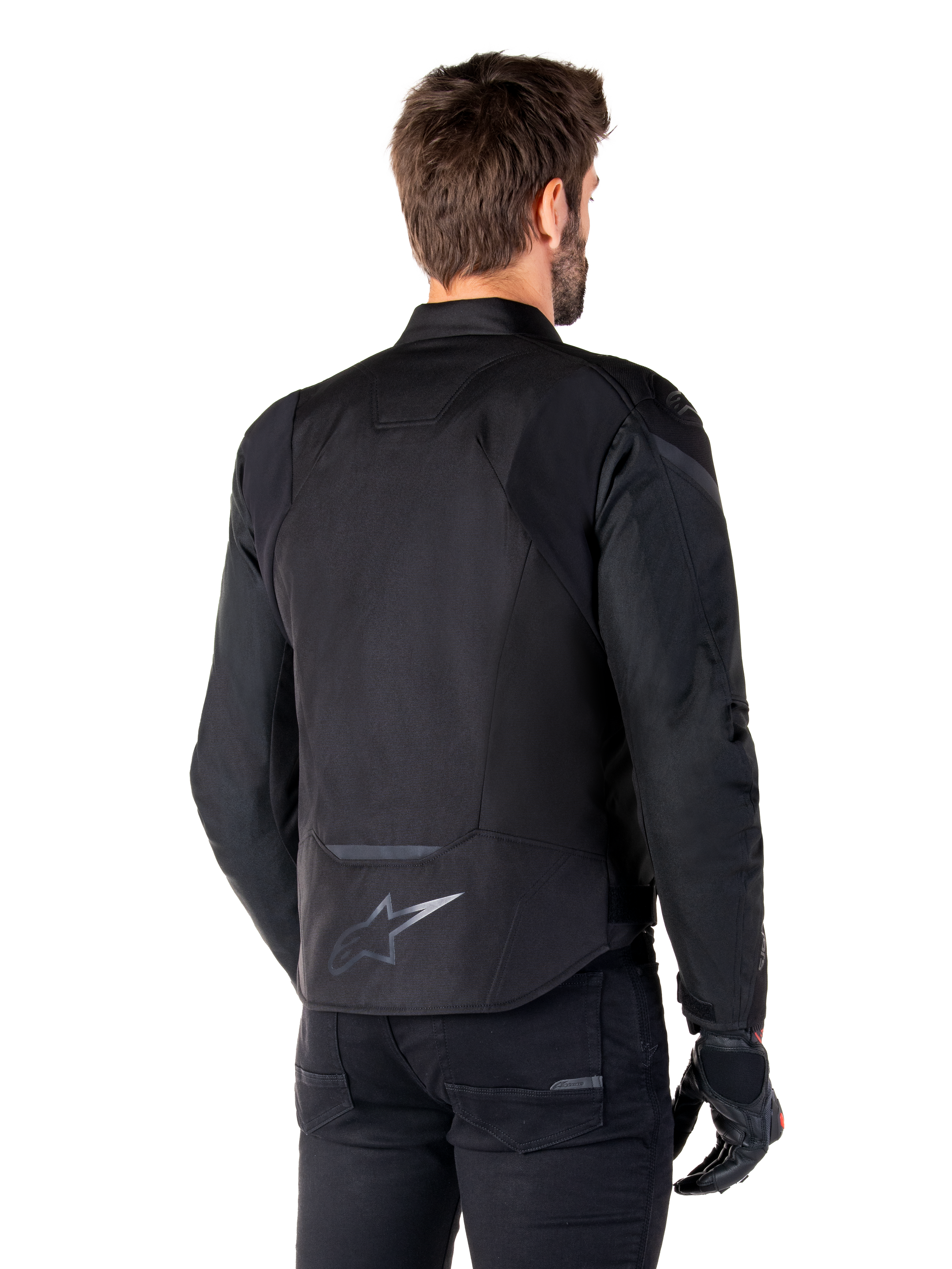 Alpinestars T-Jaws V4 Waterproof Jacket, zwart, achteraanzicht op model, met een reflecterend Alpinestars-logo op de onderrug, verlengde achterkant voor extra dekking, sportief textielontwerp met tonale panelen, gedragen met zwarte motorhandschoenen