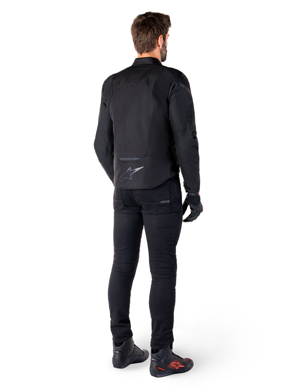 Alpinestars T-Jaws V4 Waterproof Jacket, zwart, achteraanzicht van model met zwarte motorbroek en laarzen, toont de sportieve textielconstructie en het Alpinestars-logo op de onderrug.