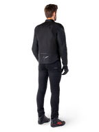 Alpinestars T-Jaws V4 Waterproof Jacket, zwart, achteraanzicht van model met zwarte motorbroek en laarzen, toont de sportieve textielconstructie en het Alpinestars-logo op de onderrug.
