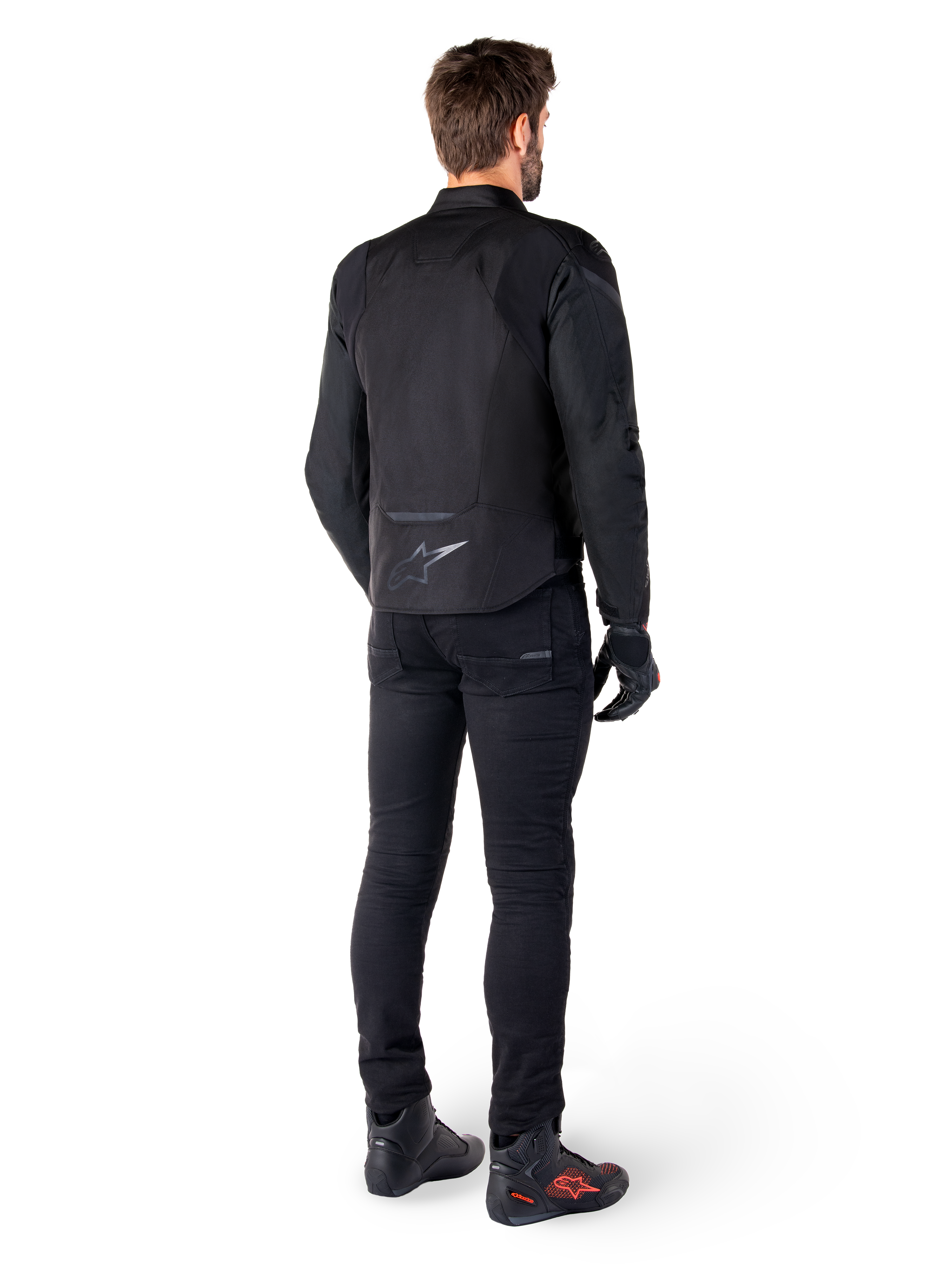 Alpinestars T-Jaws V4 Waterproof Jacket, zwart, achteraanzicht van model met zwarte motorbroek en laarzen, toont de sportieve textielconstructie en het Alpinestars-logo op de onderrug.