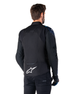 Alpinestars T-Jaws V4 Waterproof Jas, achteraanzicht, zwart met donkerblauwe en Blithe Blue accenten, wit sterlogo op de onderrug, sportief silhouet, gedragen met zwarte broek en motorhandschoenen