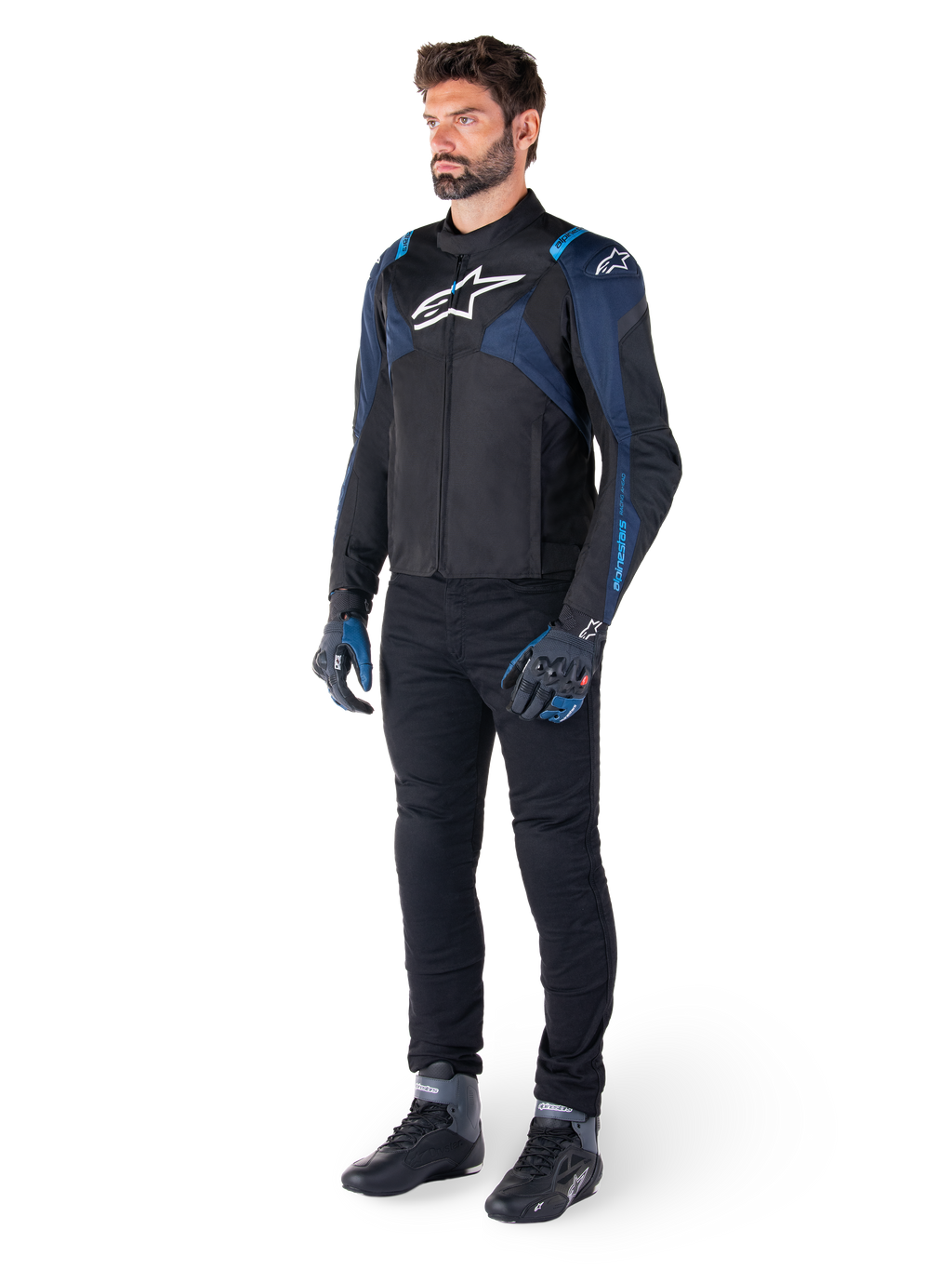 Alpinestars T-Jaws V4 Waterproof Jacket in zwart, donkerblauw en Blithe Blue, gedragen door een model met een zwarte motorbroek en motorlaarzen, voorzien van een wit Alpinestars-logo op de borst en blauwe schouderaccenten, sportieve motoruitrusting