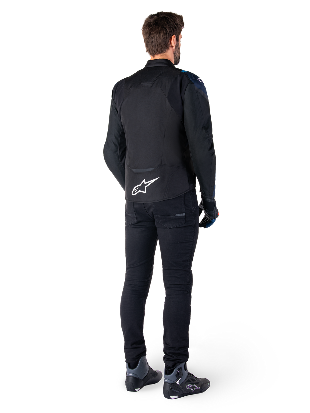Achteraanzicht van een man die het Alpinestars T-Jaws V4 Waterproof Jacket draagt in het zwart, donkerblauw en Blithe Blue, met een opvallend wit Astar-logo op de onderrug, gecombineerd met een zwarte broek en motorschoenen.