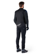 Achteraanzicht van een man die het Alpinestars T-Jaws V4 Waterproof Jacket draagt in het zwart, donkerblauw en Blithe Blue, met een opvallend wit Astar-logo op de onderrug, gecombineerd met een zwarte broek en motorschoenen.