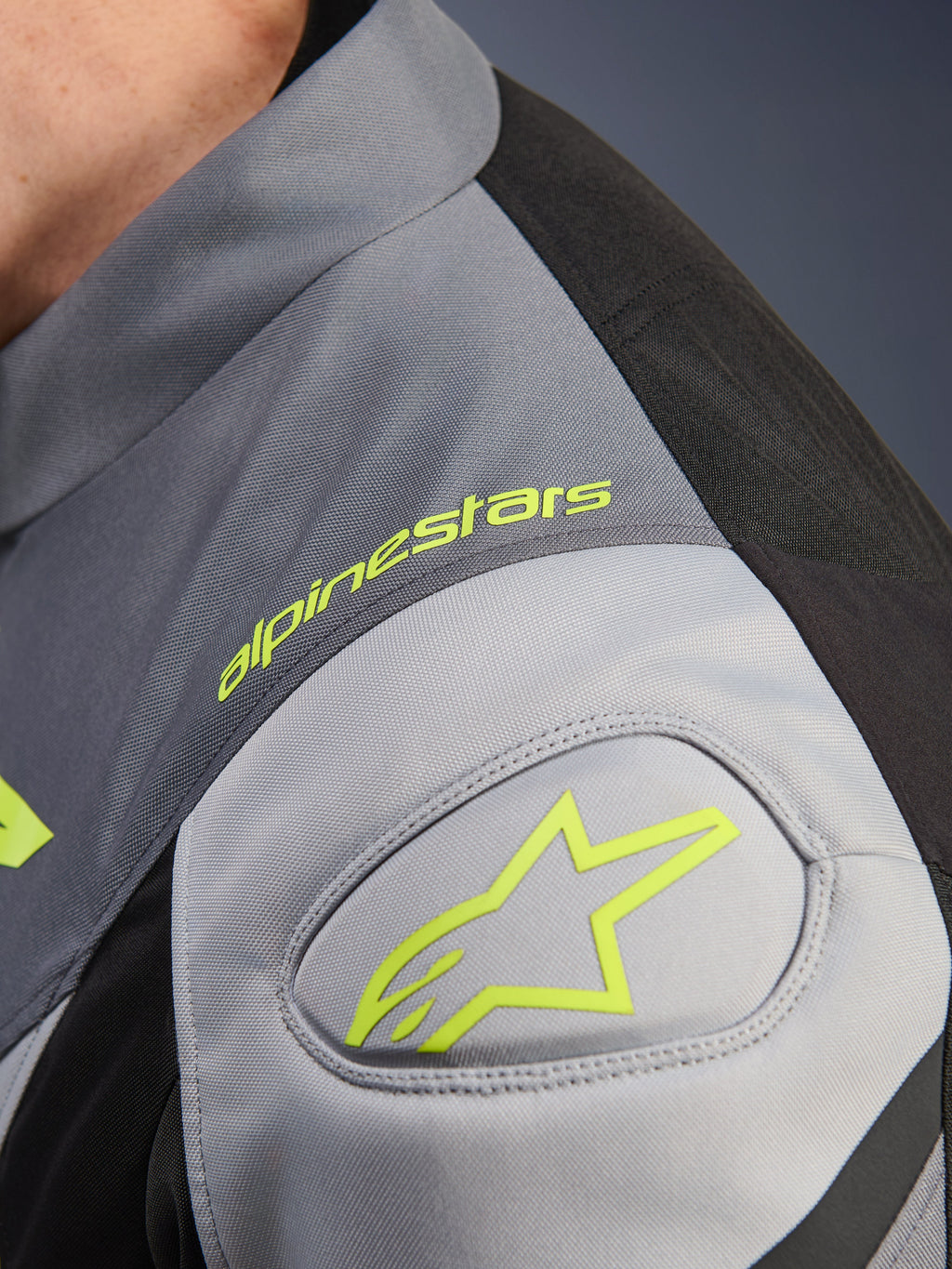 Alpinestars T-Jaws V4 Waterproof Jas, detail van de schouder met neongeel Alpinestars logo en woordmerk, Black Ice Gray en Dark Gray technisch textiel, GP Lite schouderversteviging.