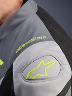 Alpinestars T-Jaws V4 Waterproof Jas, detail van de schouder met neongeel Alpinestars logo en woordmerk, Black Ice Gray en Dark Gray technisch textiel, GP Lite schouderversteviging.