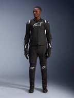 Alpinestars T-SP 1 V2 Waterproof Jacket, zwart en wit, met een opvallend wit logo op de borst en schouderaccenten, gedragen met een bijpassende zwarte motorbroek en handschoenen voor een complete wegrijlook