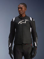 Alpinestars T-SP 1 V2 Waterproof Jacket, sportieve textiel motorjas, zwart en wit met subtiele rode details, gedragen door een mannelijk model met bijpassende handschoenen en broek, voorzien van wit Alpinestars-logo op de borst, T-SP-1-branding en beschermend silhouet voor rijden op de weg