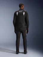 Alpinestars T-SP 1 V2 Waterproof Jacket, zwart en wit, achteraanzicht van een rijder met bijpassende zwarte motorbroek en laarzen, wit A-star-logo op de bovenrug, reflecterende schouderpanelen, sportieve textiele motorkleding