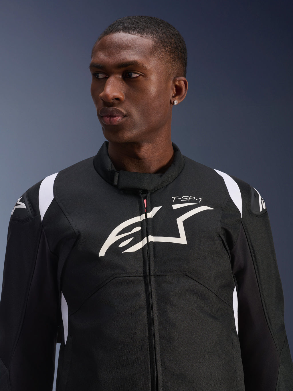 Alpinestars T-SP 1 V2 Waterproof Jacket gedragen door een model, zwart-witte textiele motorjas, groot wit Alpinestars-logo en T-SP-1-branding op de borst, sportief ontwerp met beschermende schoudersliders
