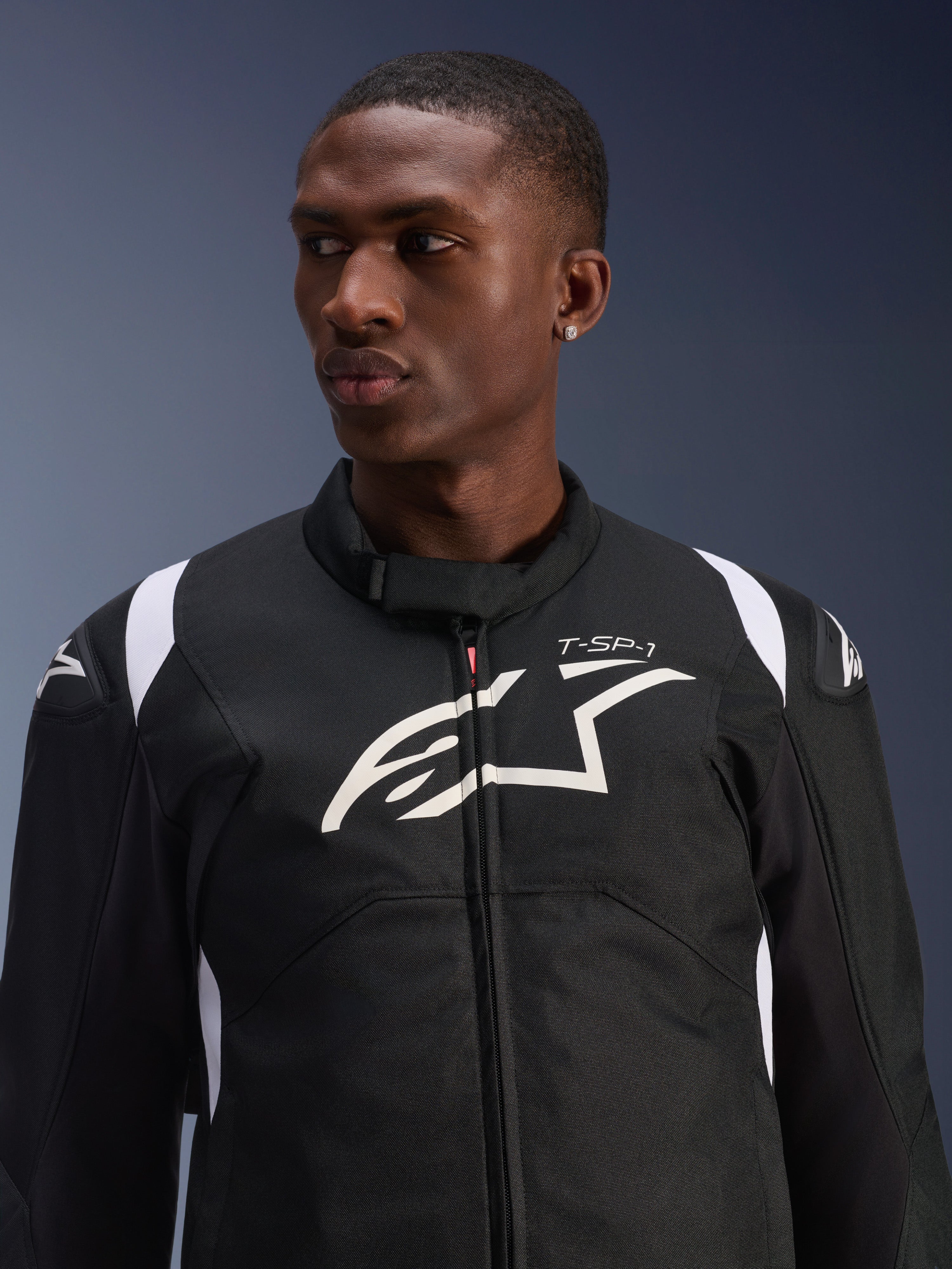 Alpinestars T-SP 1 V2 Waterproof Jacket gedragen door een model, zwart-witte textiele motorjas, groot wit Alpinestars-logo en T-SP-1-branding op de borst, sportief ontwerp met beschermende schoudersliders