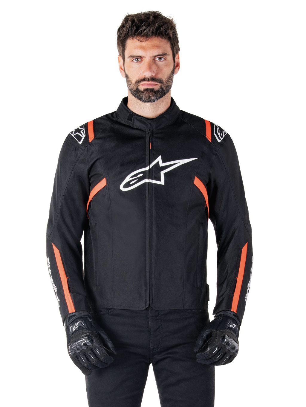Alpinestars T-SPS V2 Waterproof jas, Black White en Red Fluo, gedragen door een mannelijk model met zwarte motorhandschoenen, voorzien van een groot wit Alpinestars-logo op de borst en levendige oranje accenten op de schouders en mouwen.