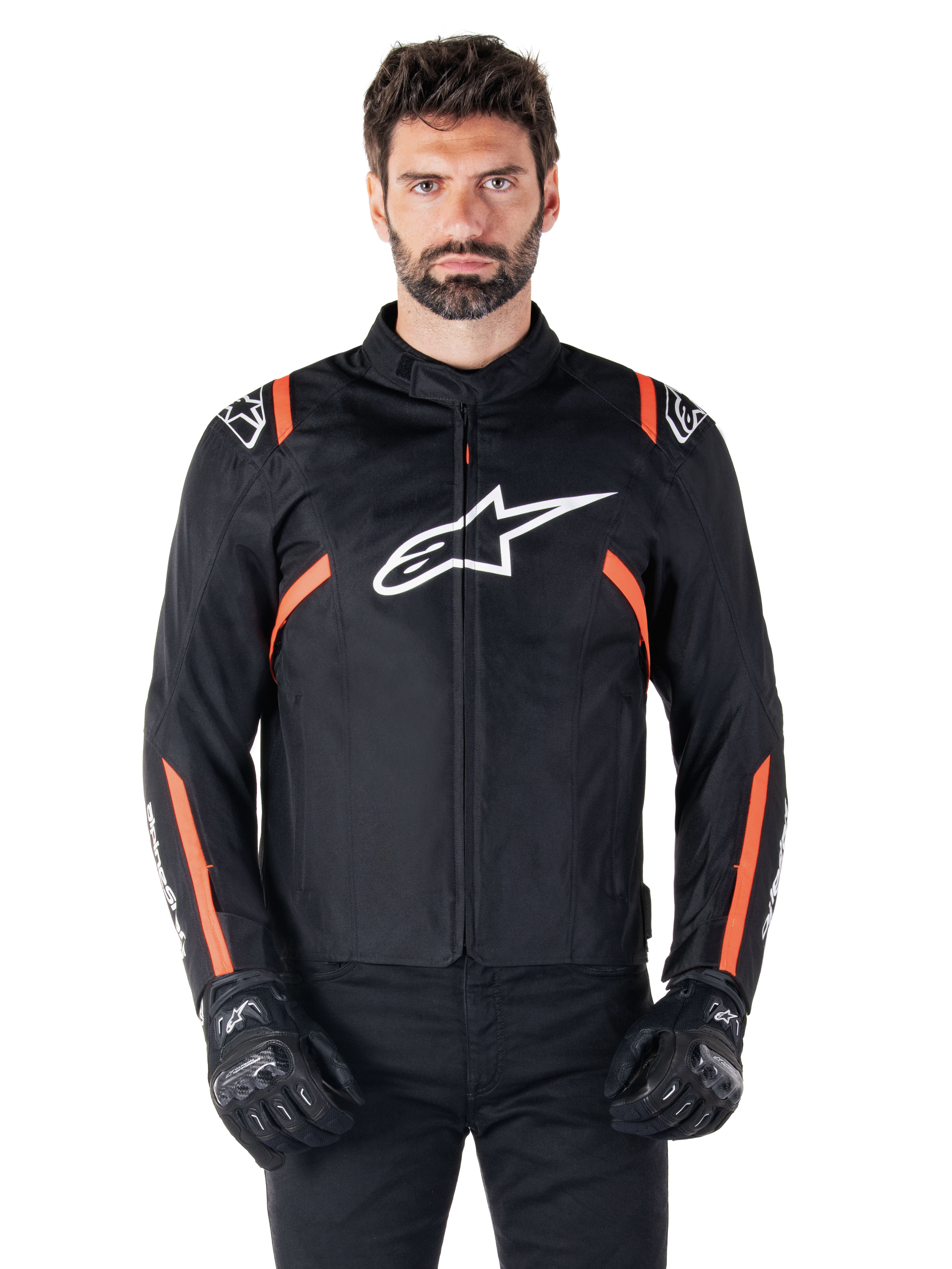 Alpinestars T-SPS V2 Waterproof jas, Black White en Red Fluo, gedragen door een mannelijk model met zwarte motorhandschoenen, voorzien van een groot wit Alpinestars-logo op de borst en levendige oranje accenten op de schouders en mouwen.