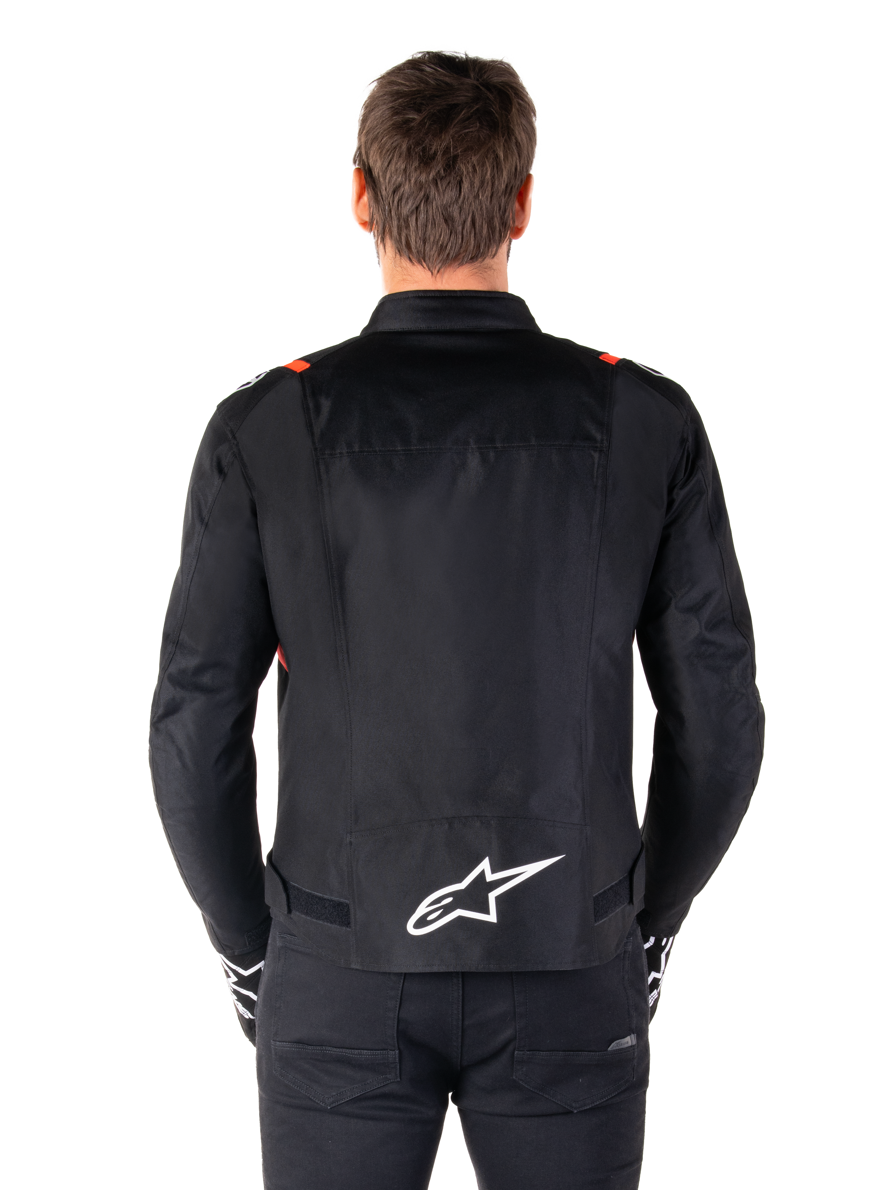 Alpinestars T-SPS V2 Waterproof Jacket, zwart met witte en rood fluo accenten, achteraanzicht met een groot wit Alpinestars-logo op de onderrug, sportieve textiel motorjas, gedragen met zwarte broek en handschoenen
