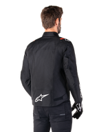 Alpinestars T-SPS V2 Waterproof Jas, Zwart Wit Rood Fluo, achteraanzicht, met wit Alpinestars-logo op de onderrug en rode accenten op de schouders, gedragen met zwarte motorhandschoenen en broek, sportieve textiele motorjas