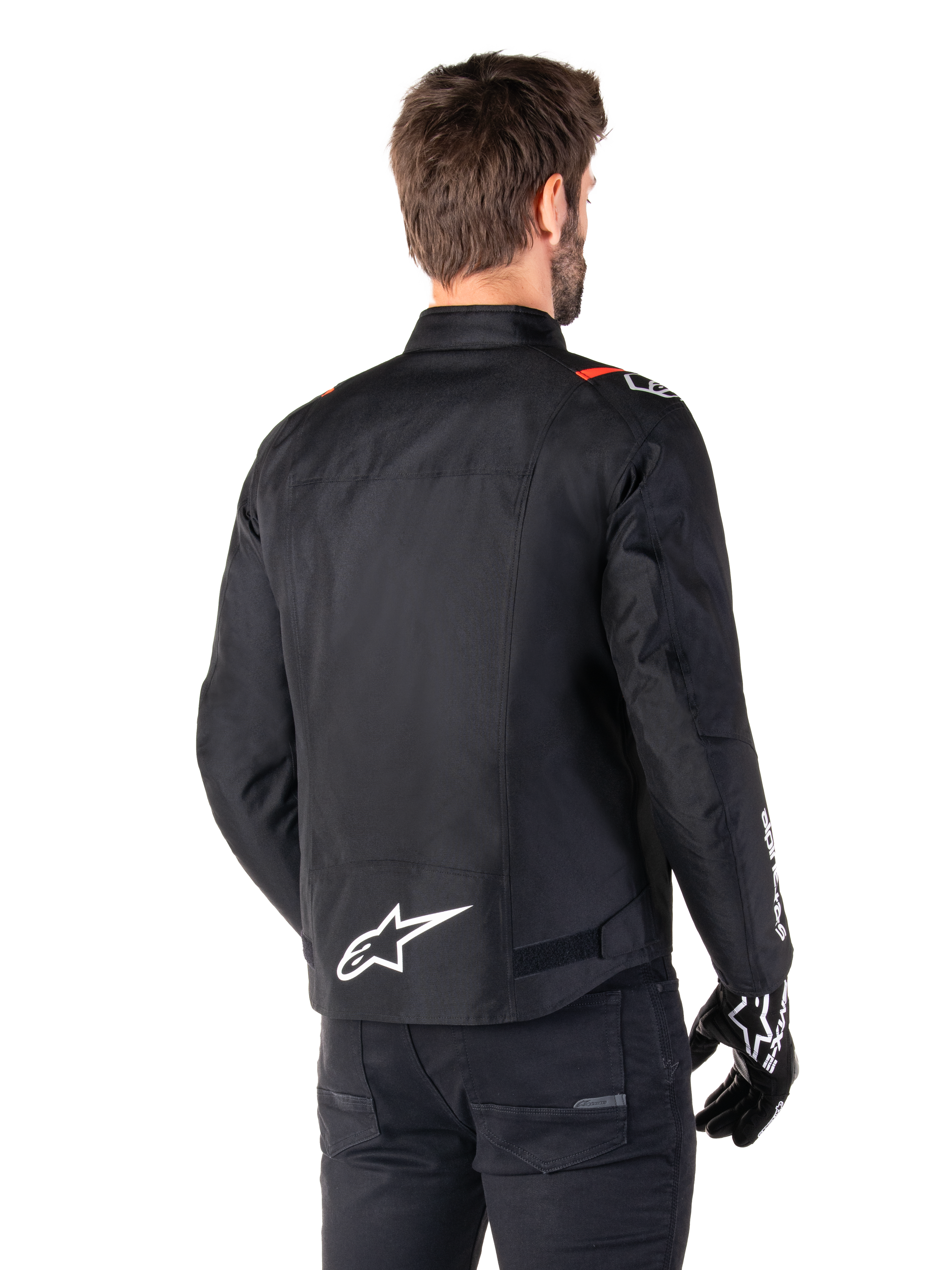 Alpinestars T-SPS V2 Waterproof Jas, Zwart Wit Rood Fluo, achteraanzicht, met wit Alpinestars-logo op de onderrug en rode accenten op de schouders, gedragen met zwarte motorhandschoenen en broek, sportieve textiele motorjas