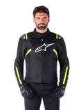 Alpinestars T-SPS V2 Waterproof Jacket, motorjas, zwart met witte en neongele accenten, gedragen door een model met zwarte handschoenen, met een wit sterlogo op de borst en neongele strepen op de mouwen en schouders, sportief gestileerde textieluitrusting voor rijden onder alle weersomstandigheden