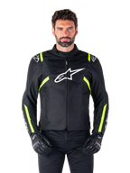Alpinestars T-SPS V2 Waterproof Jacket, motorjas, zwart met witte en neongele accenten, gedragen door een model met zwarte handschoenen, met een wit sterlogo op de borst en neongele strepen op de mouwen en schouders, sportief gestileerde textieluitrusting voor rijden onder alle weersomstandigheden