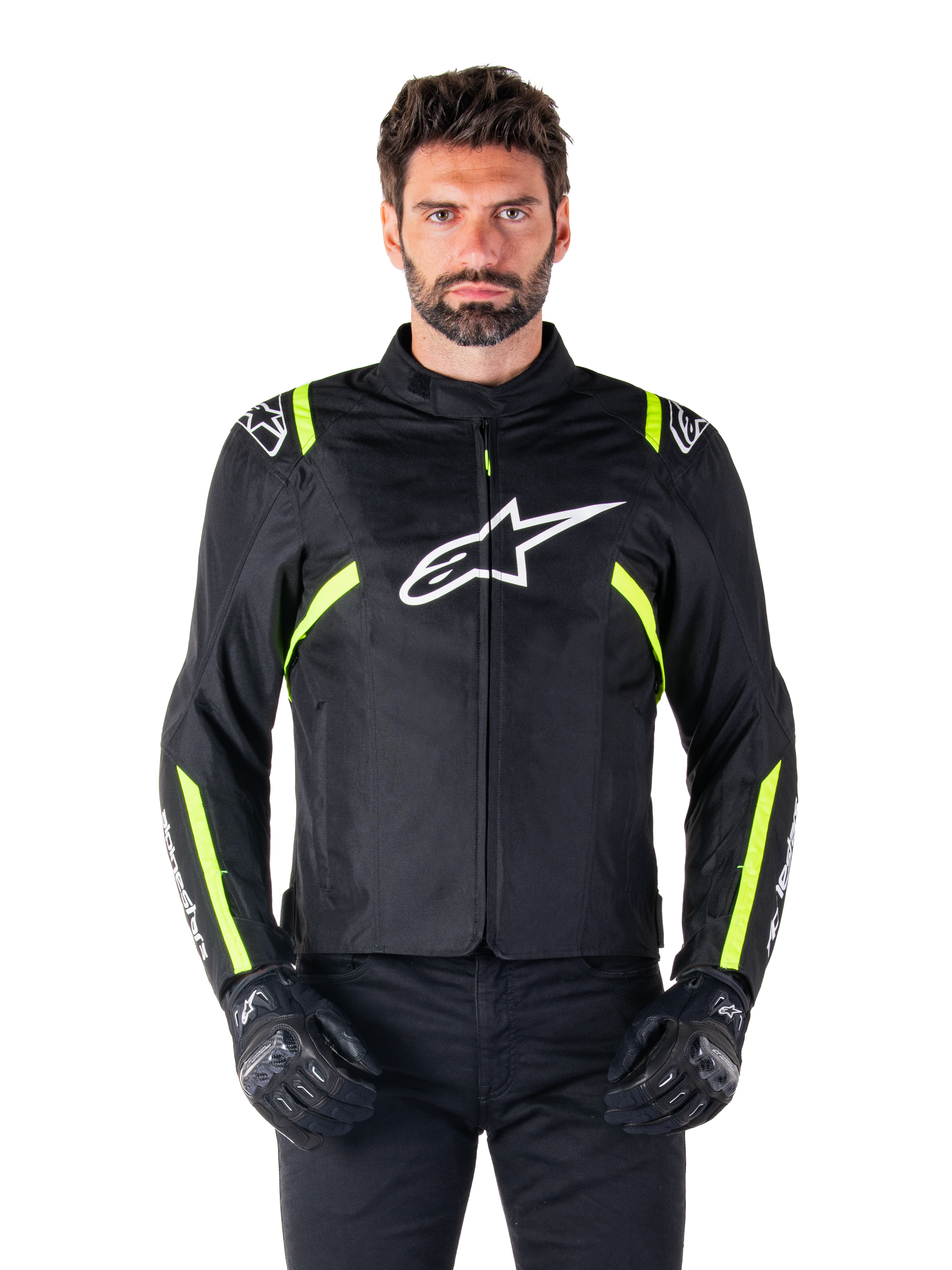 Alpinestars T-SPS V2 Waterproof Jacket, motorjas, zwart met witte en neongele accenten, gedragen door een model met zwarte handschoenen, met een wit sterlogo op de borst en neongele strepen op de mouwen en schouders, sportief gestileerde textieluitrusting voor rijden onder alle weersomstandigheden