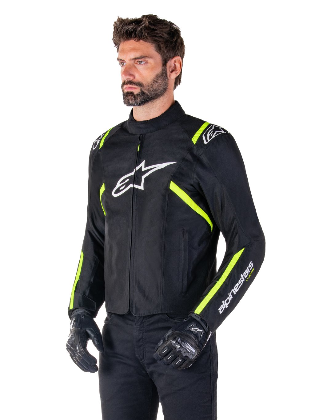 Mannelijk model draagt de Alpinestars T-SPS V2 Waterproof Jas, zwart met witte en fluorgele accenten, voorzien van een wit Astars-logo op de borst en fluorescerend gele strepen op de schouders en mouwen, gecombineerd met een zwarte broek en motorhandschoenen, sportief gesneden textiel motorjas.