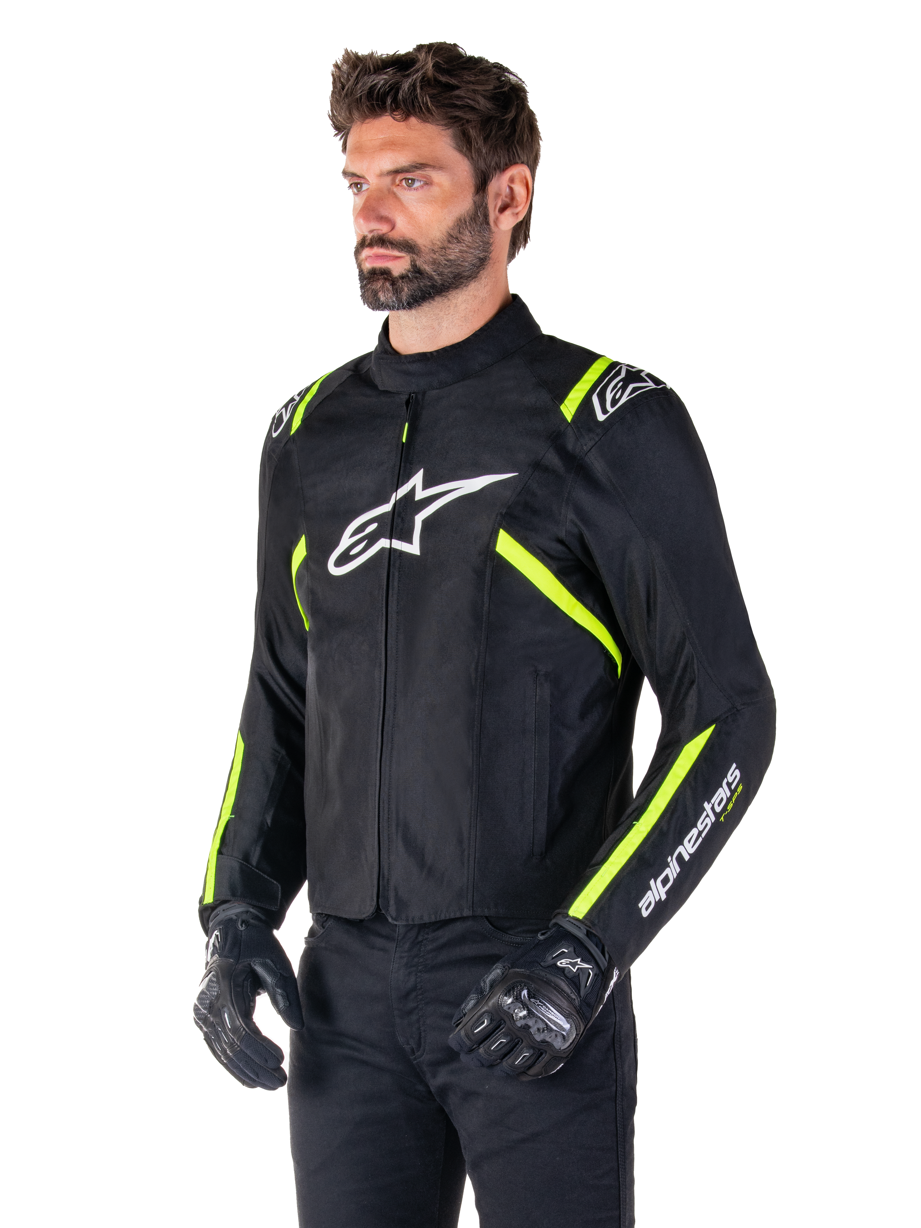 Mannelijk model draagt de Alpinestars T-SPS V2 Waterproof Jas, zwart met witte en fluorgele accenten, voorzien van een wit Astars-logo op de borst en fluorescerend gele strepen op de schouders en mouwen, gecombineerd met een zwarte broek en motorhandschoenen, sportief gesneden textiel motorjas.