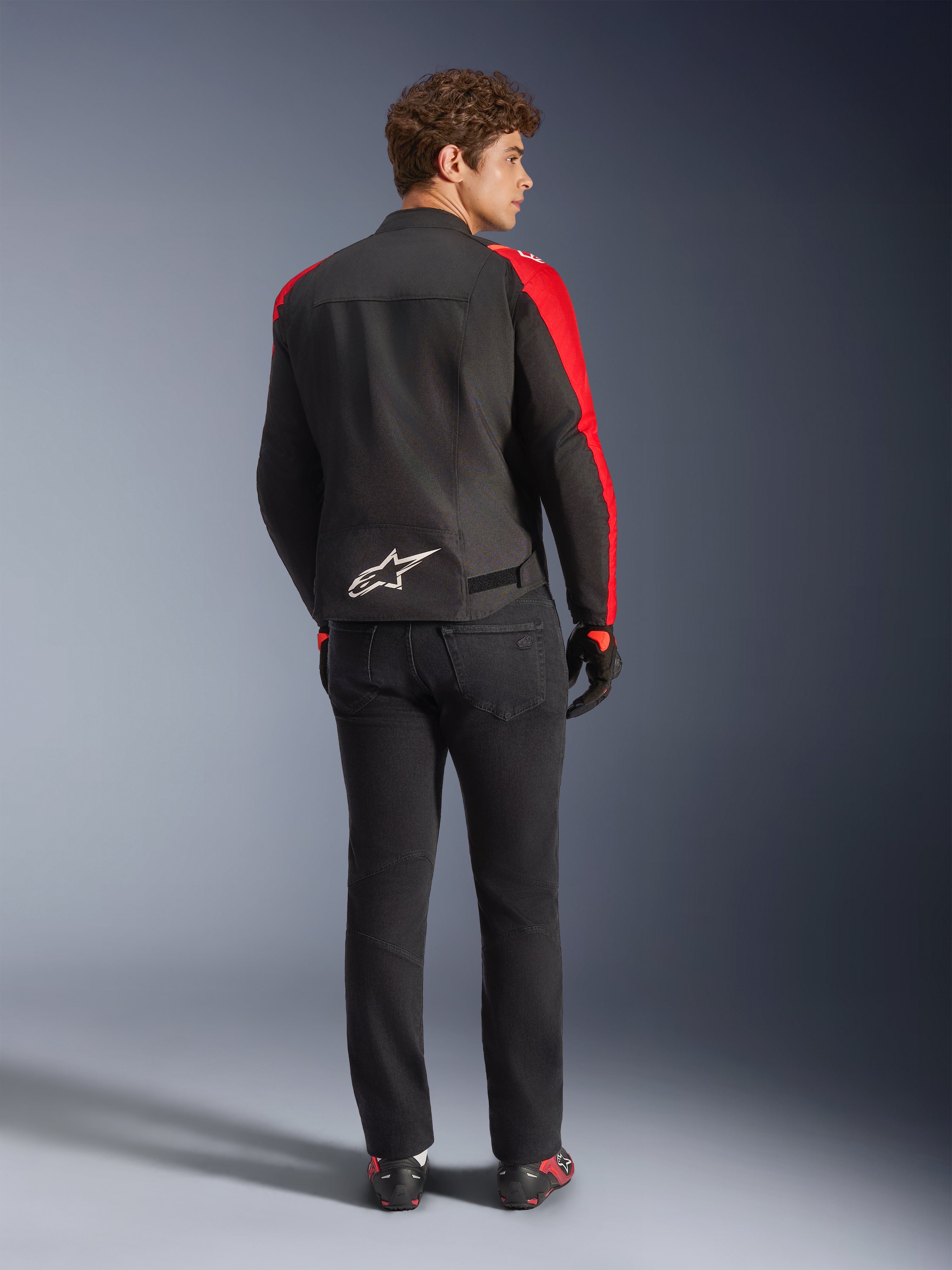 Alpinestars T-SPS V2 Waterproof Jacket, Black Red Red Fluo, back view on male model, white Alpinestars logo on the lower back, worn with black motorcycle pants and gloves, sporty textile waterproof riding jacket