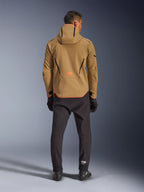 Alpinestars Aeroshell Waterproof Jacket in Dark Khaki Black Orange Fluo, achteraanzicht van een man die de softshell-jas met capuchon draagt, voorzien van zwarte biesjes en een oranje logo, gecombineerd met een zwarte technische broek en handschoenen.