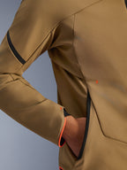 Close-up van de Alpinestars Aeroshell waterdichte jas, Dark Khaki met zwarte en fluo oranje accenten, detail van de verborgen handzak met rits en de mouwboord, stretch softshell textiel voor motorrijden