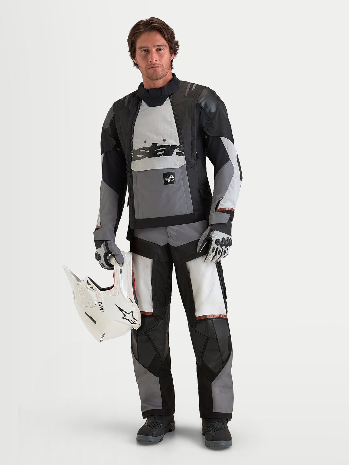Alpinestars Harok V2 Drystar Gear Set, adventure touring motorcycle gear set in black, gray, and white, front studio view of a model wearing the waterproof jacket and matching pants while holding a white helmet.