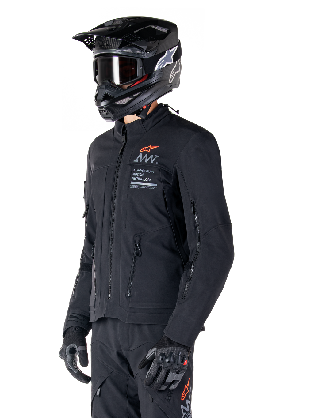 Alpinestars AMT-8 Stretch Drystar® XF Jas, zwart, gedragen door een motorrijder met bijpassende adventure broek en handschoenen, voorzien van een zwarte motorcrosshelm en bril, ventilatieopeningen met rits op de borst en mouwen, Alpinestars Motion Technology branding met een oranje logo, premium adventure-touring uitrusting