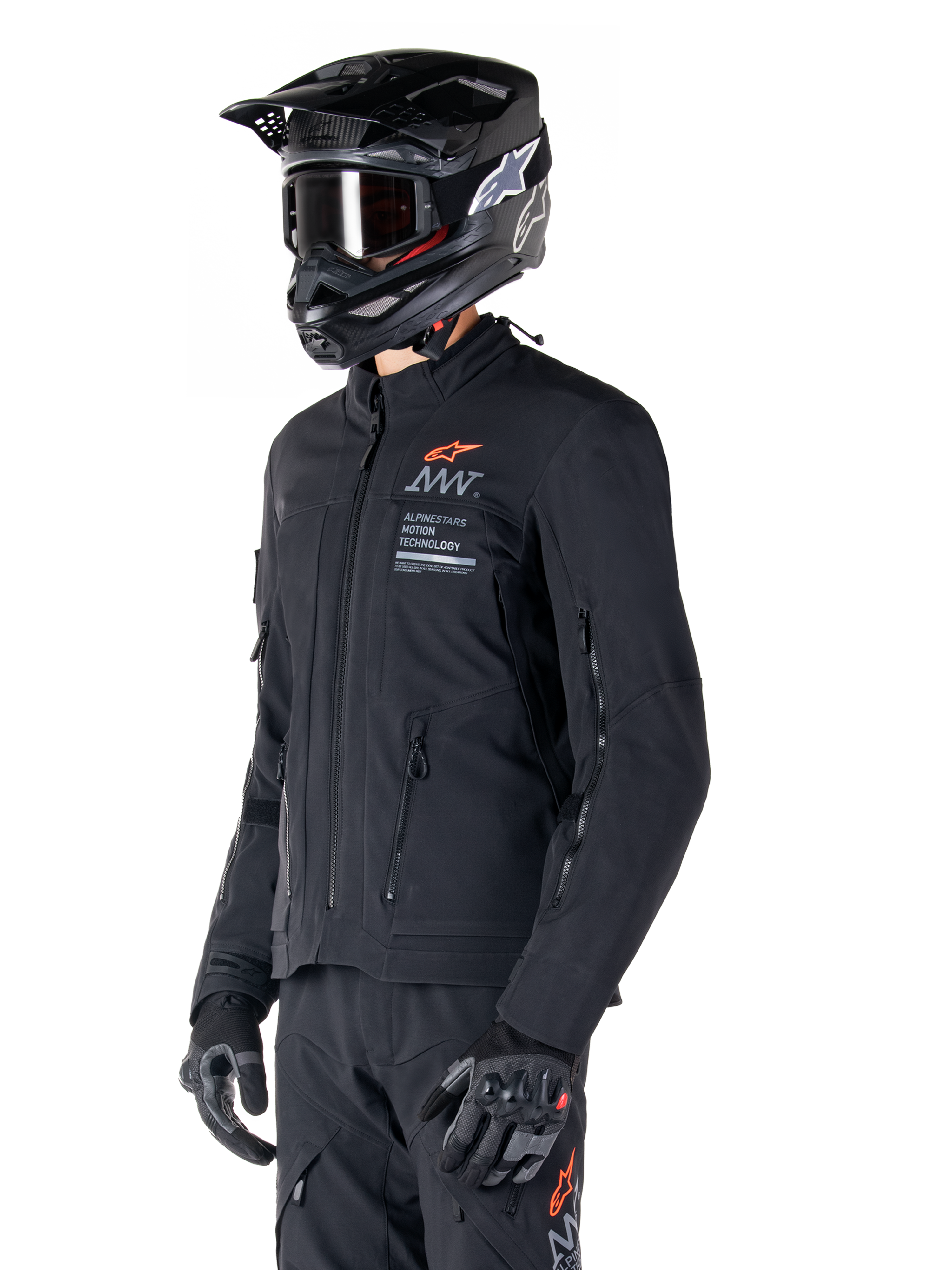 Alpinestars AMT-8 Stretch Drystar® XF Jas, zwart, gedragen door een motorrijder met bijpassende adventure broek en handschoenen, voorzien van een zwarte motorcrosshelm en bril, ventilatieopeningen met rits op de borst en mouwen, Alpinestars Motion Technology branding met een oranje logo, premium adventure-touring uitrusting