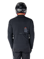 Alpinestars AMT-8 Stretch Drystar® XF Jas, achteraanzicht, zwart, gedragen met een zwarte helm en broek, met Alpinestars Motion Technology-branding op de rug, adventure touring-ontwerp met ergonomisch stretchmateriaal.