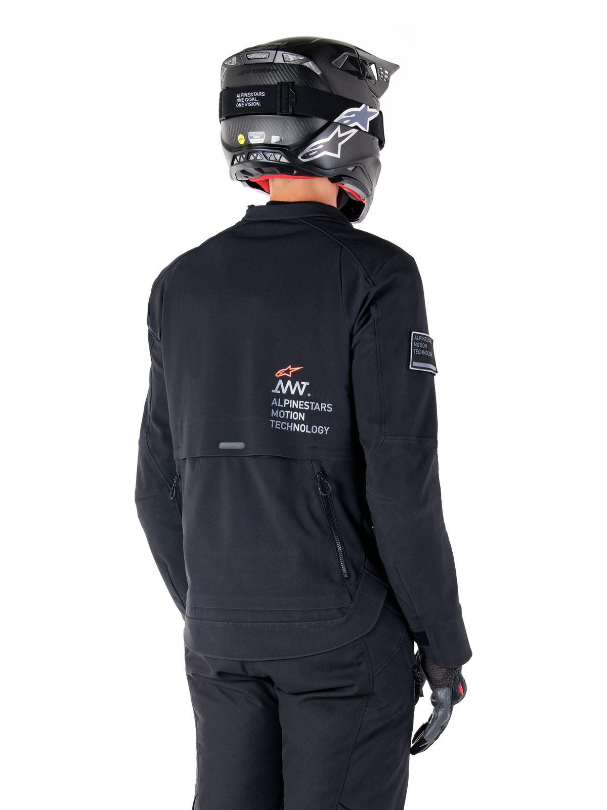 Achteraanzicht van een motorrijder die de zwarte Alpinestars AMT-8 Stretch Drystar® XF Jas draagt, voorzien van 'AMT Alpinestars Motion Technology' branding op de rug, technische ventilatie met ritssluiting, gecombineerd met een zwarte motorhelm en handschoenen