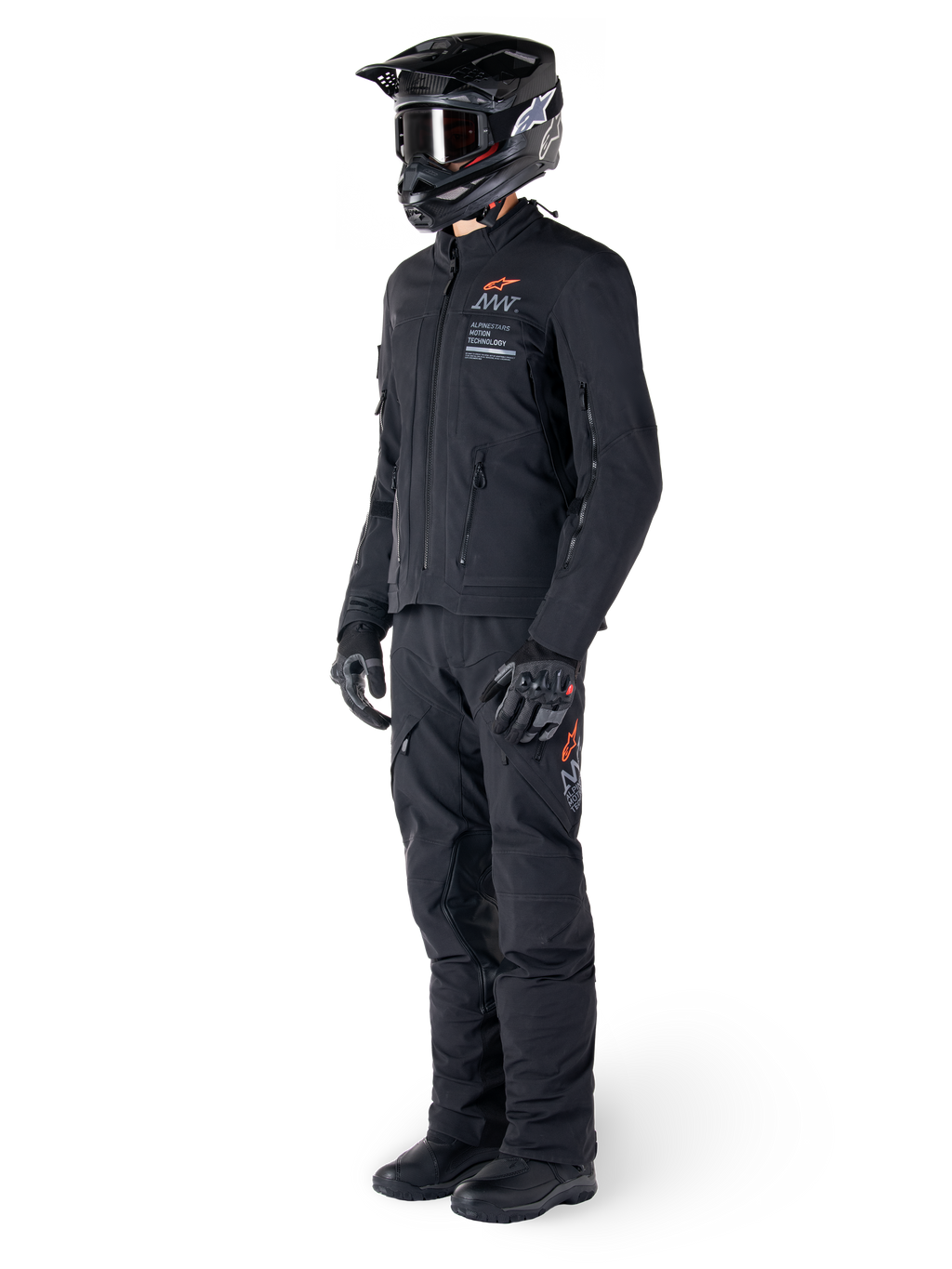 Alpinestars AMT-8 Stretch Drystar® XF jas, adventure motorjas, zwart, gedragen met bijpassende broek, helm en handschoenen, voorzien van Alpinestars Motion Technology branding met oranje accenten, duurzame stretchconstructie voor adventure rijden