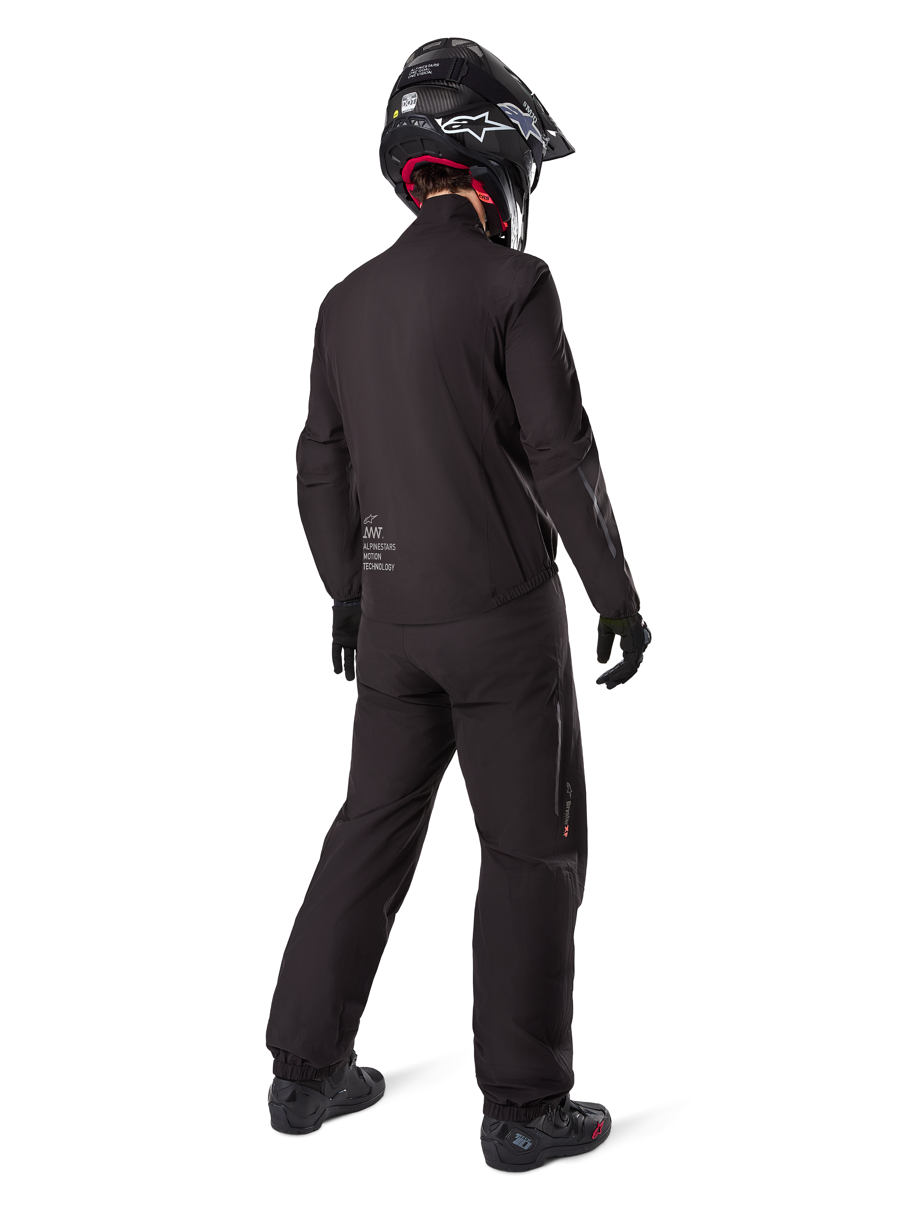 Achteraanzicht van een motorrijder die de Alpinestars AMT-8 Stretch Drystar® XF jasvoering draagt, zwarte technische motorkleding, gedragen met bijpassende broek en zwarte helm, met "AMT Alpinestars Motion Technology" branding op de rug, strak minimalistisch ontwerp voor adventure touring