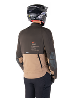 Alpinestars AMT-8 Stretch Drystar® XF Jas, adventure motorjas, donkerbruin en donkerkhaki, achteraanzicht met AMT Alpinestars Motion Technology branding, tweekleurig textielontwerp met ventilatieritsen op de rug en dakpanontwerp, gedragen met zwarte helm en motorbroek