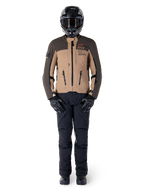 Alpinestars AMT-8 Stretch Drystar® XF Jas, adventure motorjas, donkerbruin en donkerkhaki, gedragen met een zwarte helm, motorbril, zwarte handschoenen, zwarte broek en zwarte laarzen, voorzien van ventilatieopeningen op de borst en AMT-branding, gecoördineerde uitrusting voor adventure touring