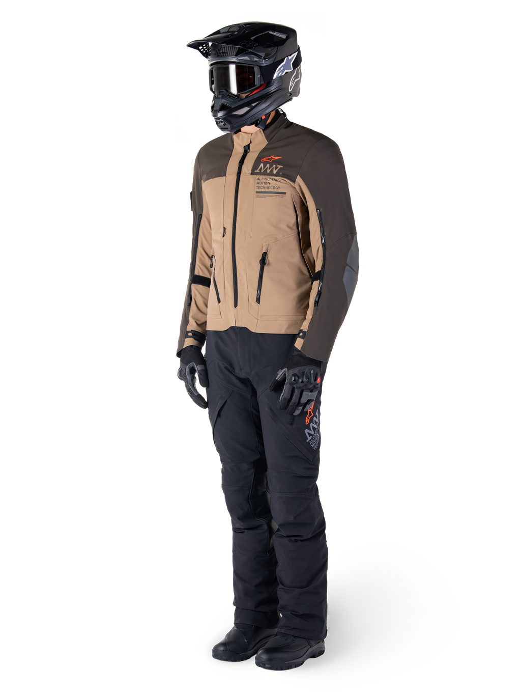 Adventure-motorrijder in volledige uitrusting, Alpinestars AMT-8 Stretch Drystar® XF Jas in donkerbruin en donkerkhaki, gecombineerd met zwarte adventure-broek, zwarte helm, handschoenen en laarzen, voorzien van oranje AMT-branding en technische ventilatieritsen voor touring over lange afstanden