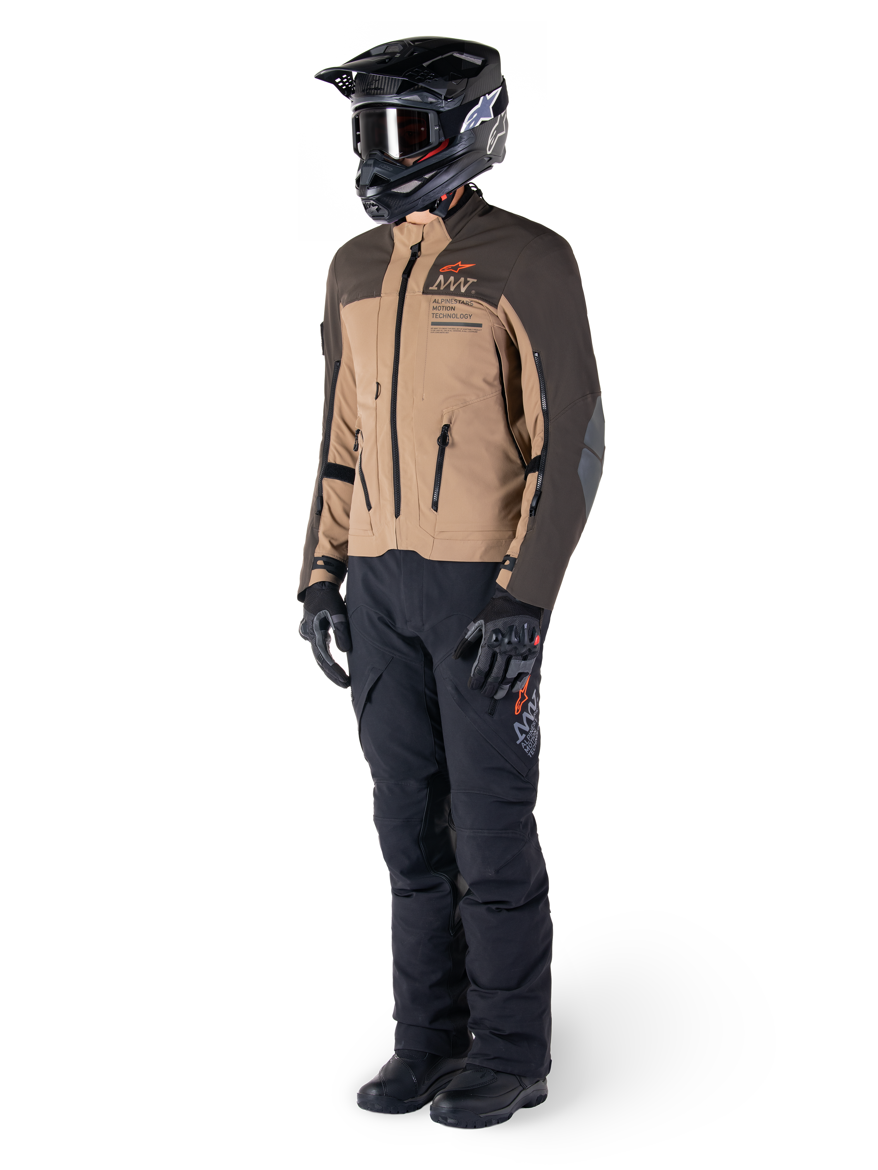 Adventure-motorrijder in volledige uitrusting, Alpinestars AMT-8 Stretch Drystar® XF Jas in donkerbruin en donkerkhaki, gecombineerd met zwarte adventure-broek, zwarte helm, handschoenen en laarzen, voorzien van oranje AMT-branding en technische ventilatieritsen voor touring over lange afstanden